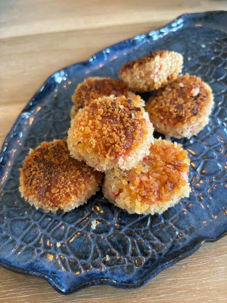 Sprøde krabbedeller med gylden panko-panering serveret på et mørkeblåt keramisk fad.